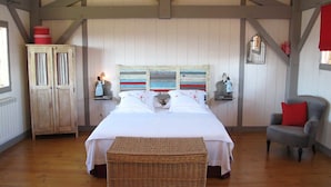 Une chambre à coucher avec un grand lit, une commode, un banc en osier et une chaise rouge.