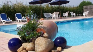 Une piscine entourée de verdure et de rochers décoratifs, avec des chaises longues et des parasols.