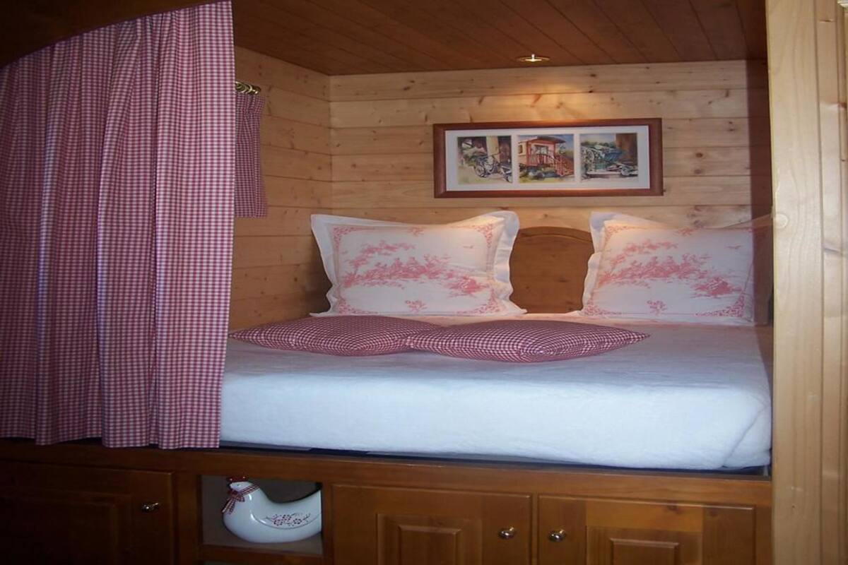 Een houten kamer met een bed, een geruit gordijn en een lijst met een afbeelding.