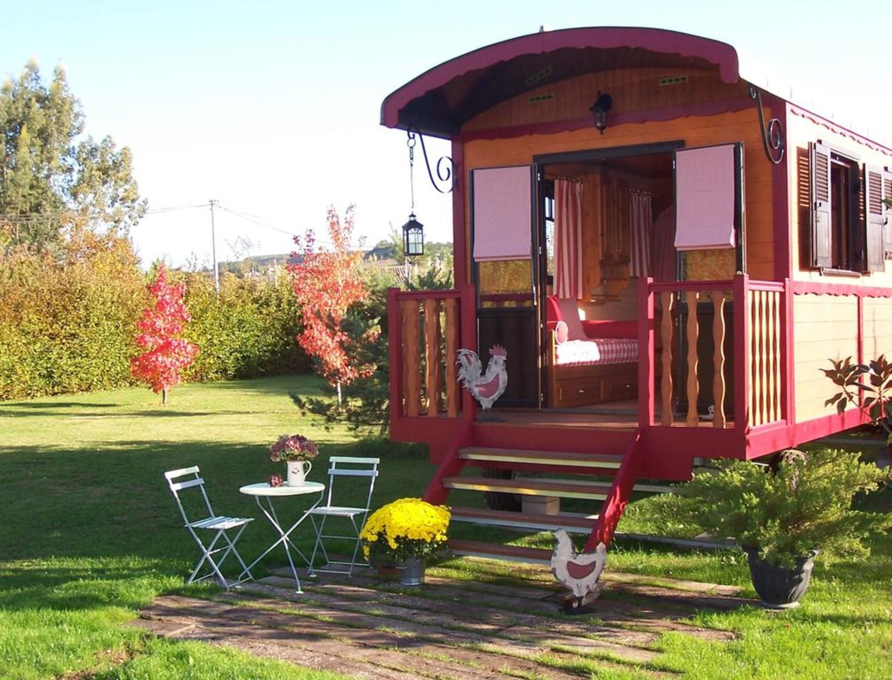 A wooden cabin with a porch, a bed, and a dining area with chairs and a table.