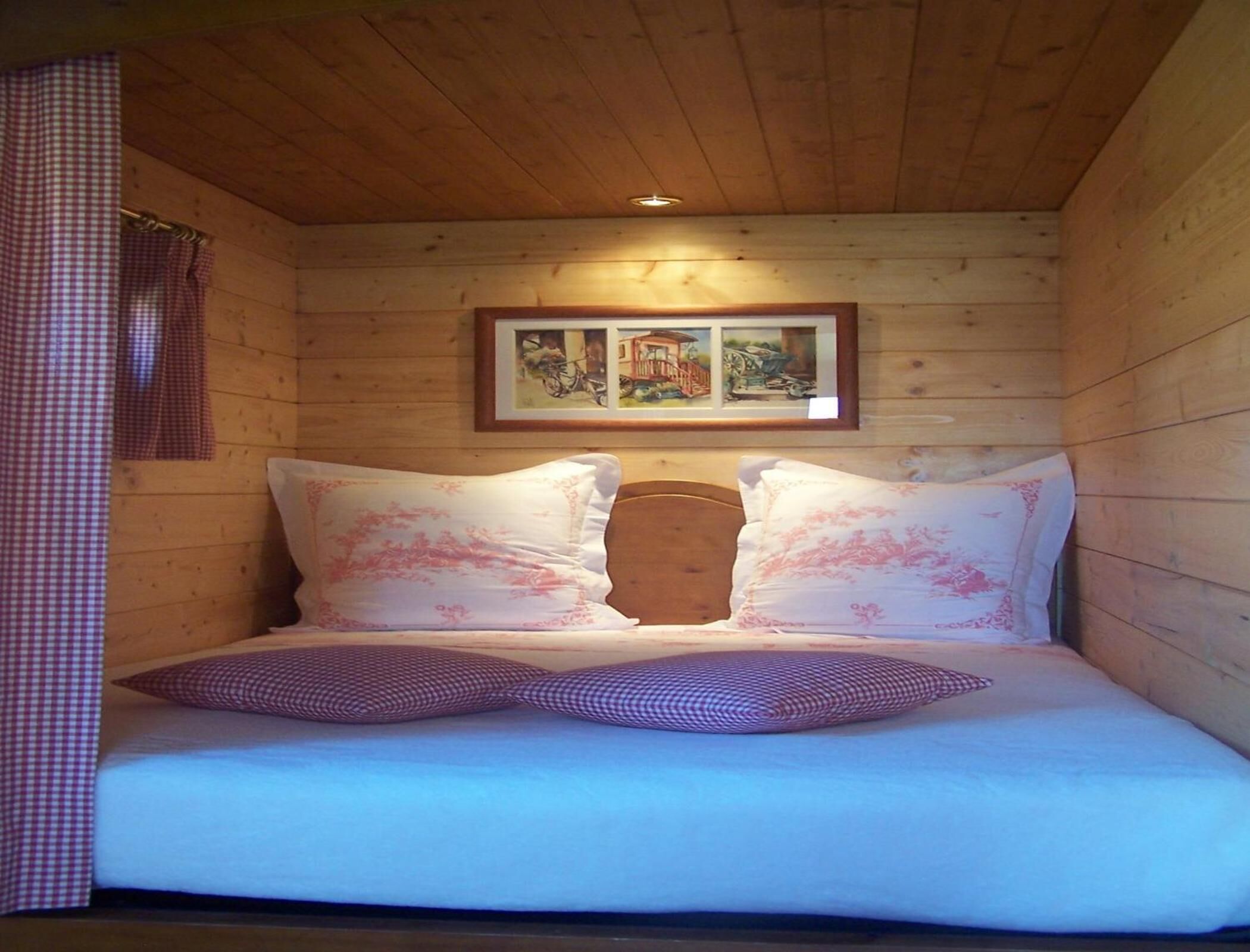 A wooden cabin room with a bed, checkered curtains, and a framed picture on the wall.