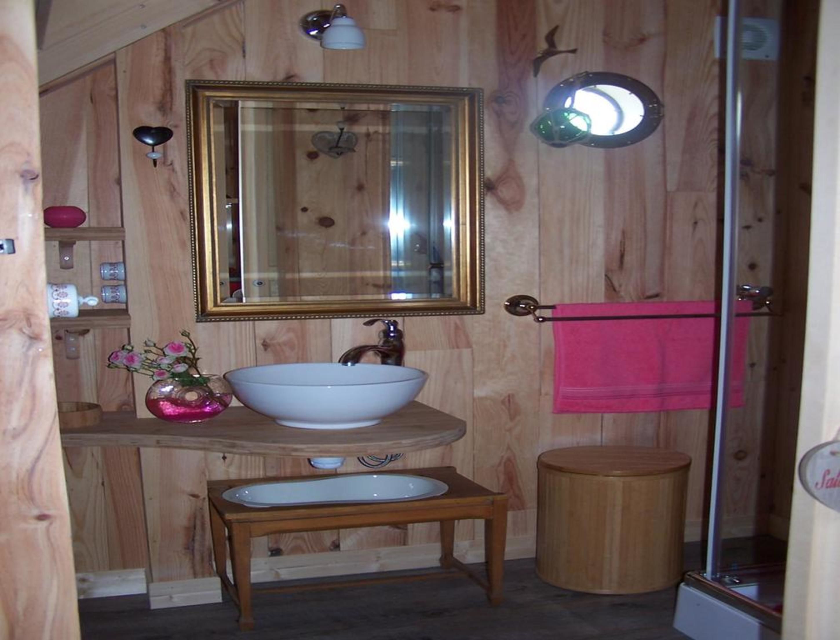 Un baño de madera con un espejo grande, un lavabo blanco, una mesita pequeña y un cubo de basura de madera.