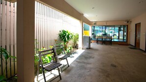 Un espacio interior amplio con piso de concreto, un banco de madera y un ventanal de vidrio que da a un área exterior con plantas y una mesa.