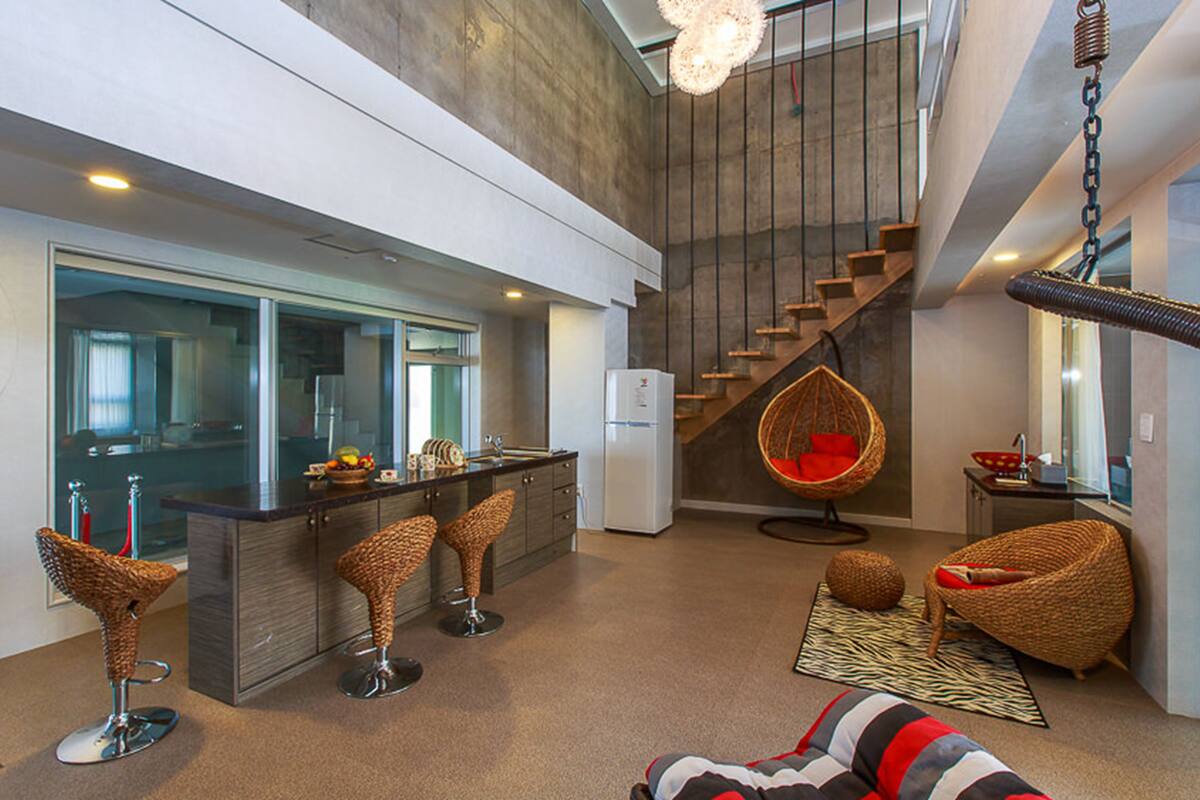 Una cocina moderna con una isla central, un comedor con taburetes de bar, una silla colgante y una escalera.