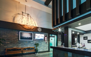 A lobby with a wooden bench, a wall-mounted TV, a bicycle light fixture, and a reception desk with computers. - Bato Resort (Geoje)