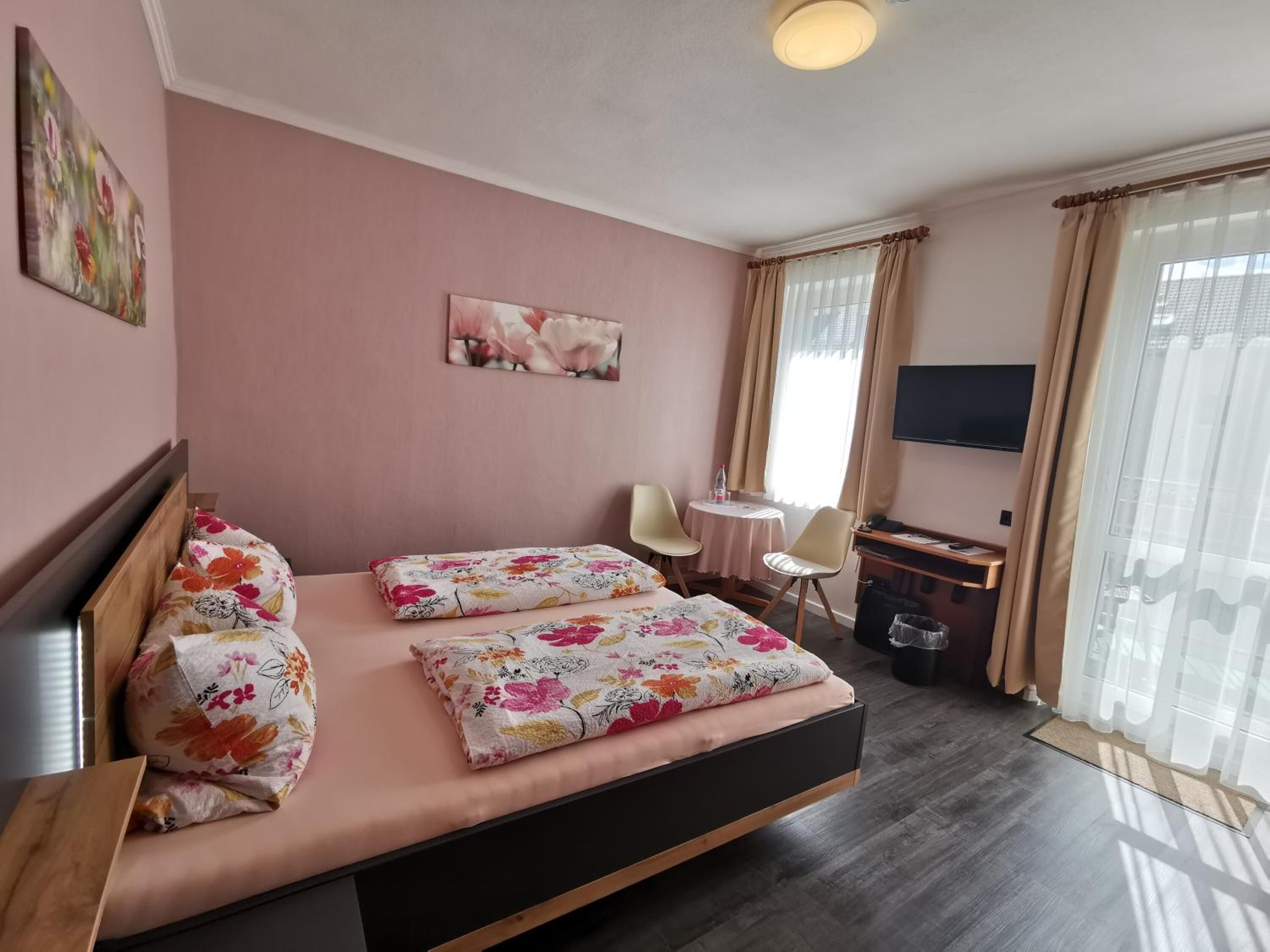 Habitación de hotel con cama, dos sillas, una mesita, televisión y ventana con cortinas.