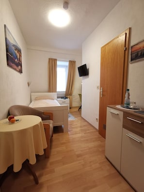 A compact hotel room with a bed, bedside table, and a small kitchenette.