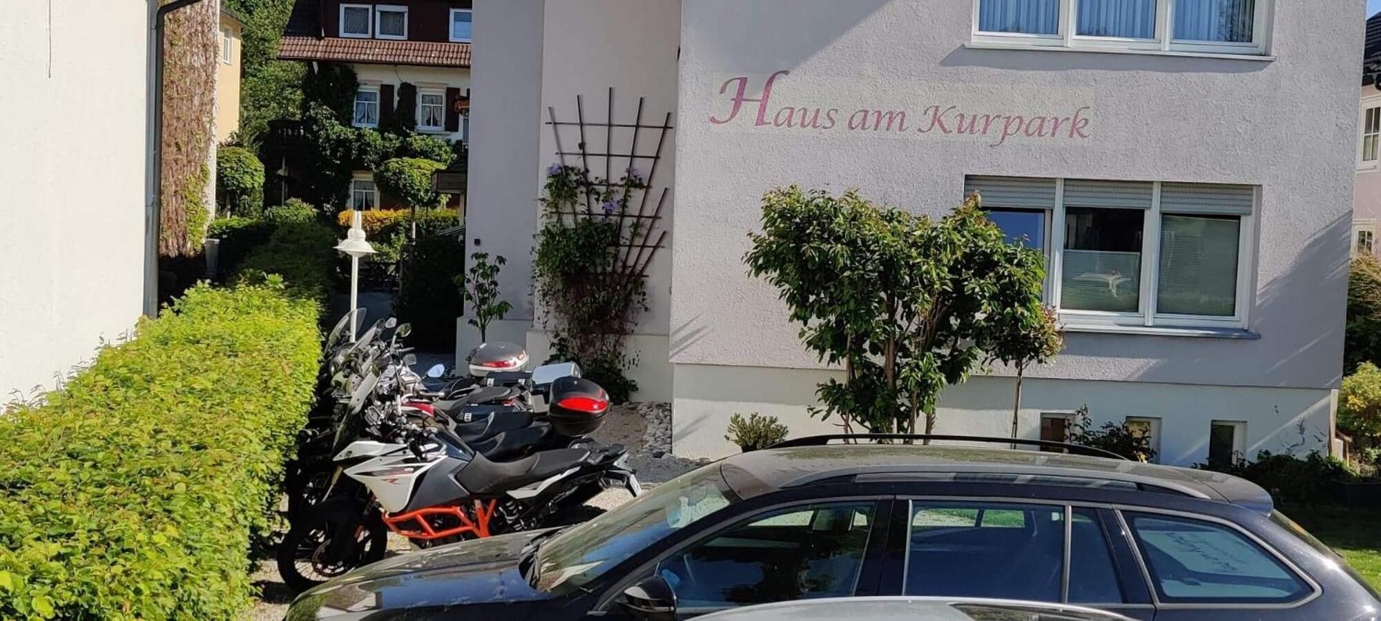 Rakennuksessa on kyltti, jossa lukee ”Haus am Kurpark”, ja sen edessä on rivi parkkeerattuja moottoripyöriä.