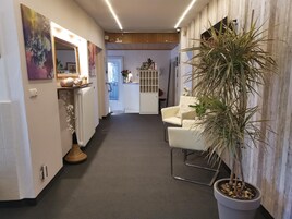 A hallway with a radiator, a potted plant, a white chair, and a cabinet with decorative items.