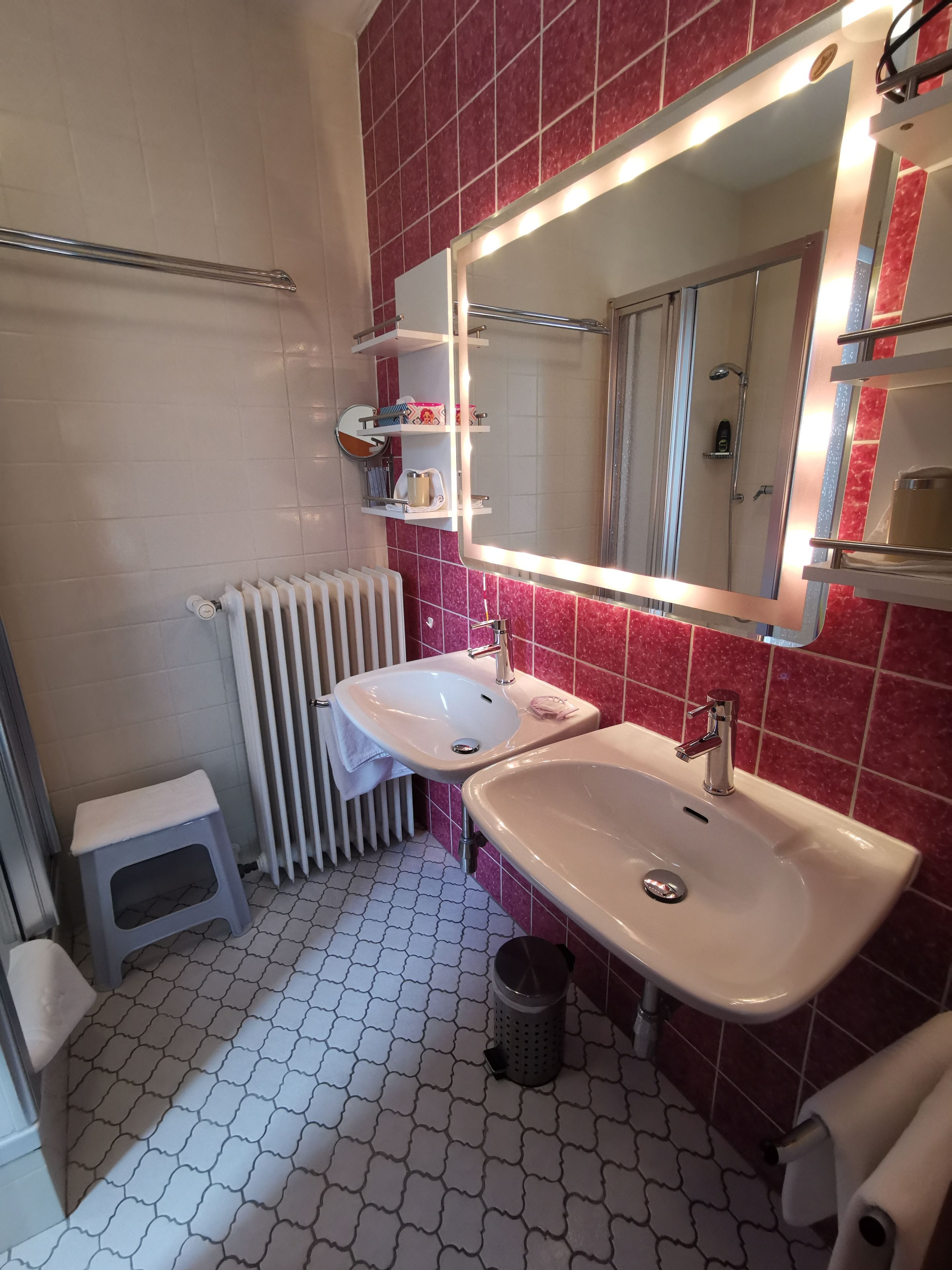 Et badeværelse med to håndvaske, et spejl, en radiator og en lille skammel.