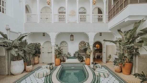 Une cour intérieure avec une piscine centrale, des plantes en pot et un sol carrelé.