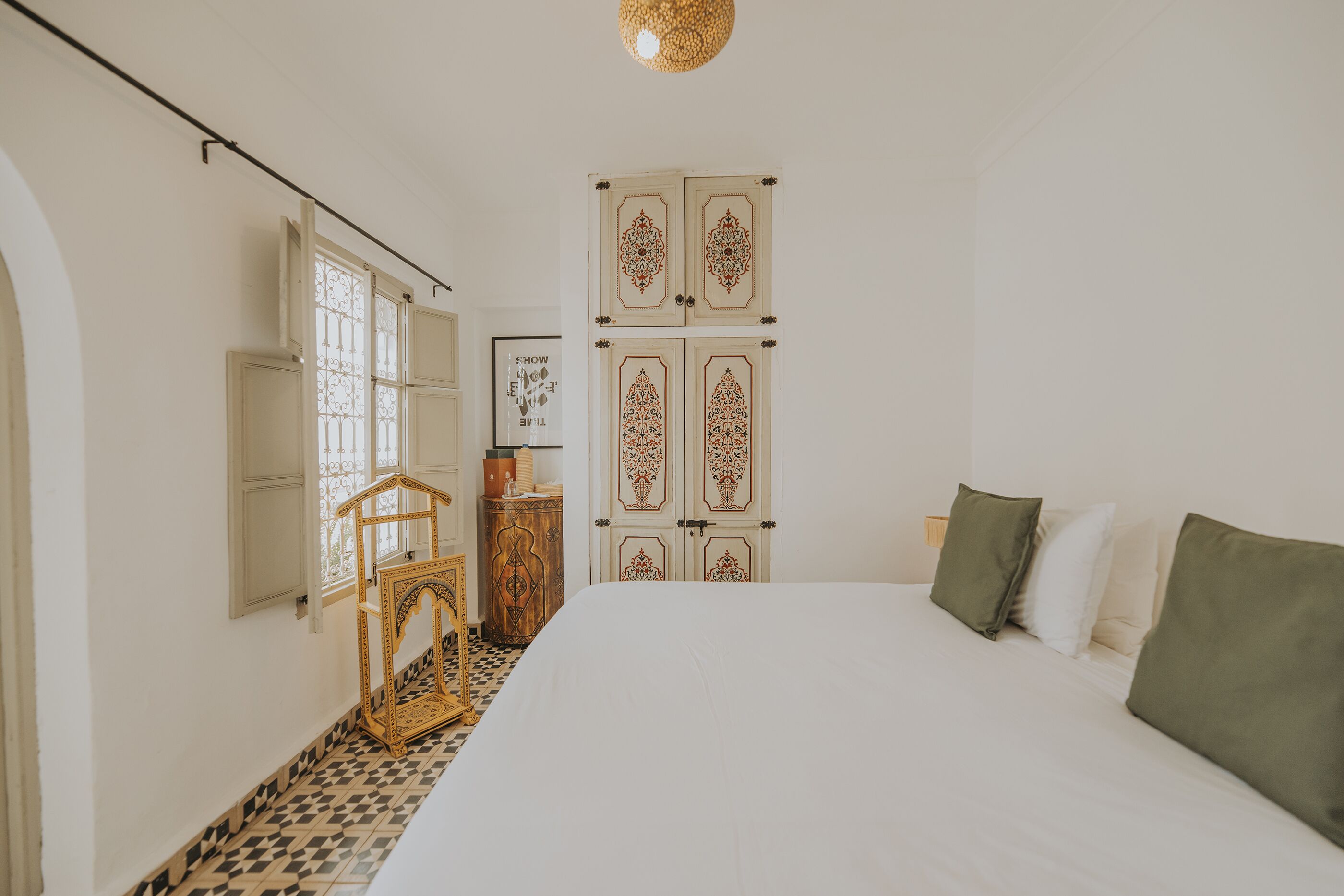 Un dormitorio con una cama grande, un armario con paneles decorativos, una mesita con lámpara y un suelo estampado.
