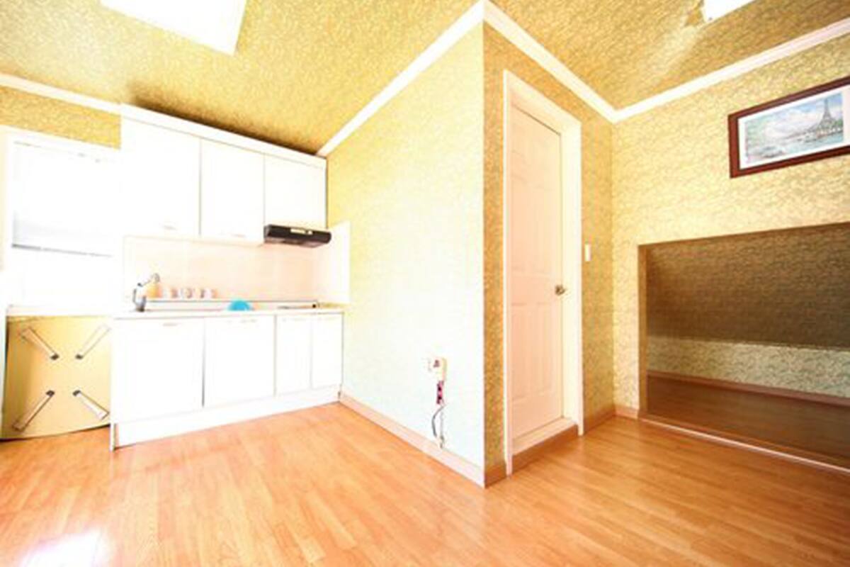 A room with a wooden floor, white cabinets, a door, and a framed picture on the wall.