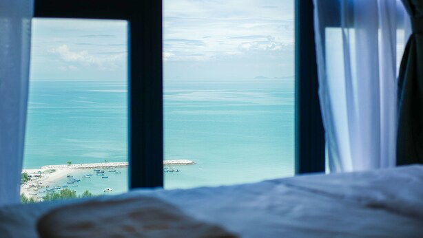 A view from a window overlooking a beach with boats and a distant island. - May Full Seaview Luxury Suite (George Town)