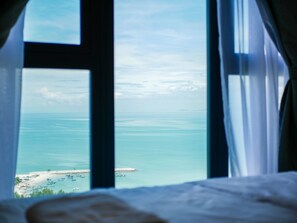 A view from a window overlooking a beach with boats and a distant island. - May Full Seaview Luxury Suite (George Town)