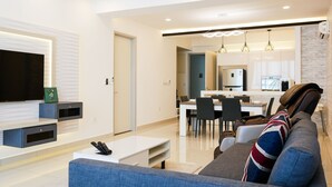 A modern living room with a sofa, coffee table, and TV. There is a dining area with chairs and a kitchen in the background. - May Full Seaview Luxury Suite (George Town)