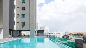 A rooftop swimming pool with a wooden deck, surrounded by modern buildings and a clear sky. - May Full Seaview Luxury Suite (George Town)