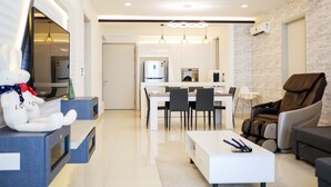 A modern living room with a sofa, a massage chair, a dining area with a table and chairs, and a kitchen in the background. - May Full Seaview Luxury Suite (George Town)