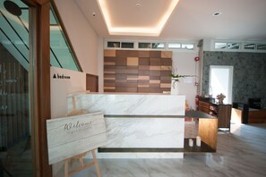 A modern hotel lobby with a marble reception desk, a wooden accent wall, and a staircase leading to the upper floor. - Jowa Hotel (Chiang Mai)