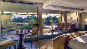 A tented room with a bed, a table, and chairs, and a view of the outdoors. - Ngerende in the Wild Riverview (Maasai Mara)