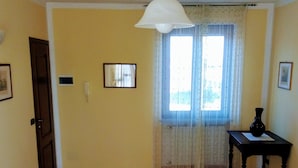 A dining area with a wooden table and two white chairs, a hanging light fixture, and a window with curtains. - Bed & Breakfast Cascina Bellezza (Poirino)