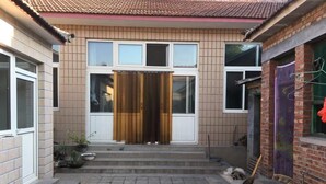 A two-story house with a tiled roof, a front door with a curtain, and a small front yard with steps leading to the entrance. - Guo House (Changping)