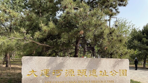 A stone sign with gold lettering in a park with pine trees and a person in the background. - Guo House (Changping)