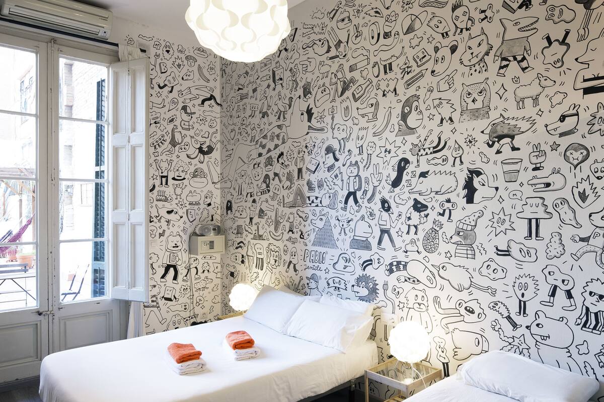 Een slaapkamer met twee bedden, witte lakens en een muur vol zwart-wit tekeningen.
