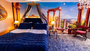 A bedroom with a four-poster bed, a view of ancient ruins through a large window, and a balcony with a red chair. - Hotel Slottsgården (Vadstena)