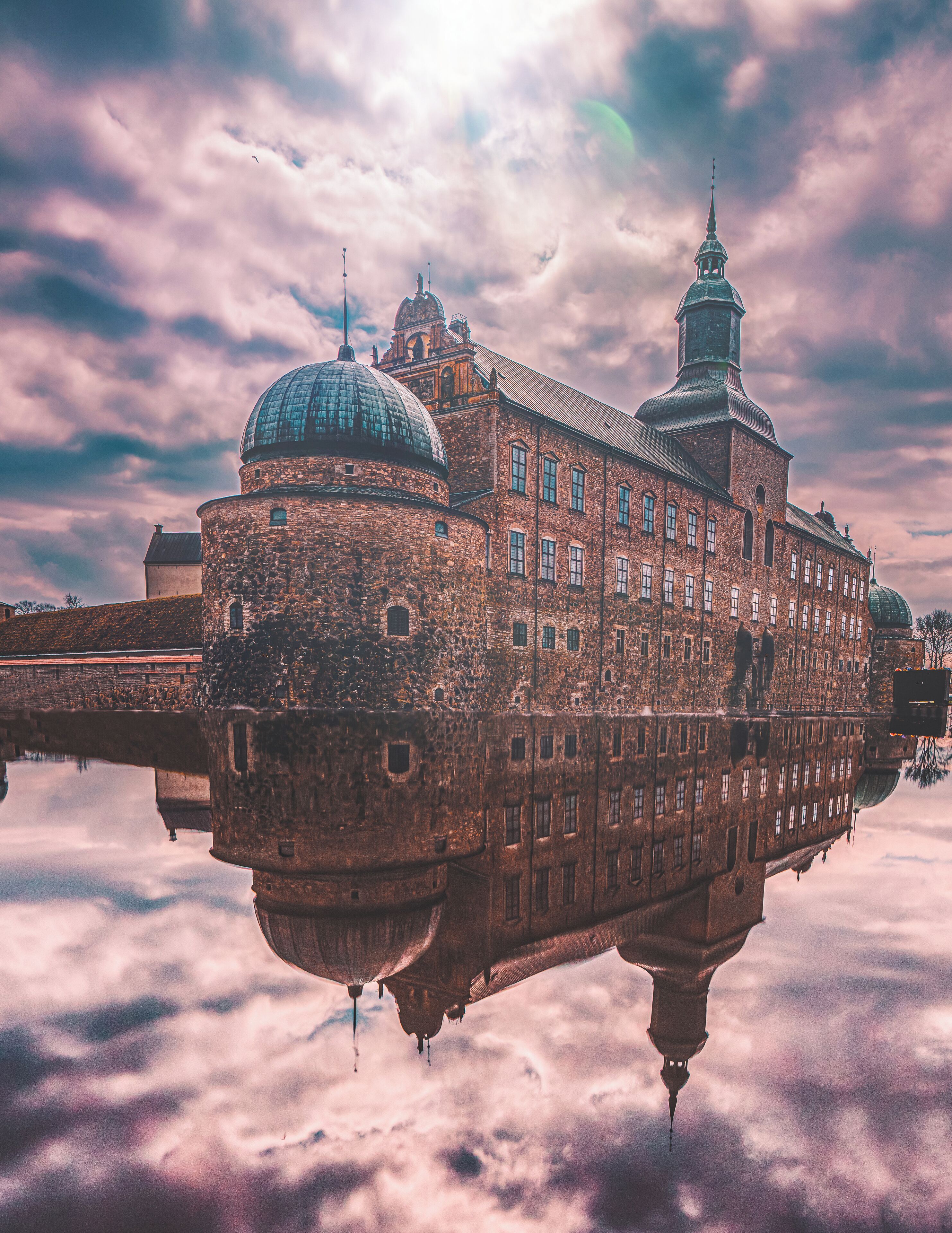 A historic building with a prominent dome and a tall tower, reflected in a body of water.
