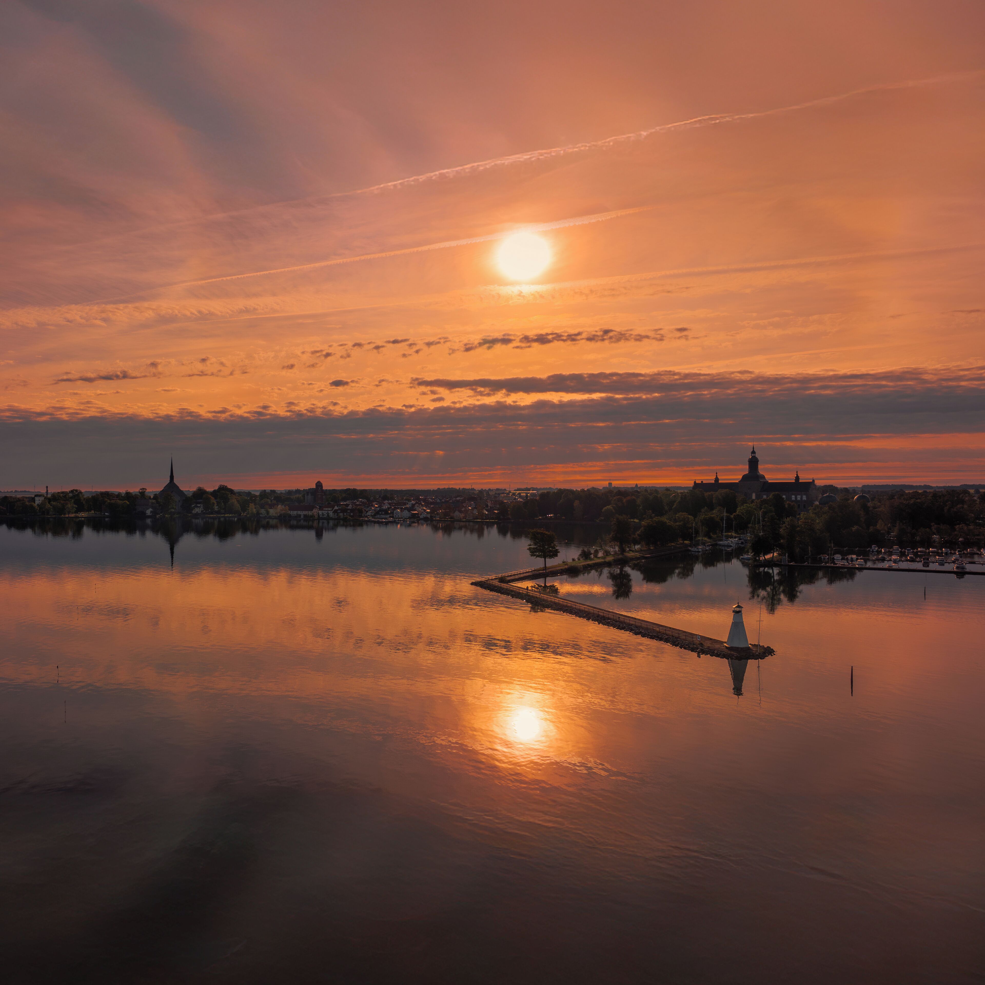 Een kalm meer dat de zonsondergang weerspiegelt, met een brug en gebouwen in de verte.
