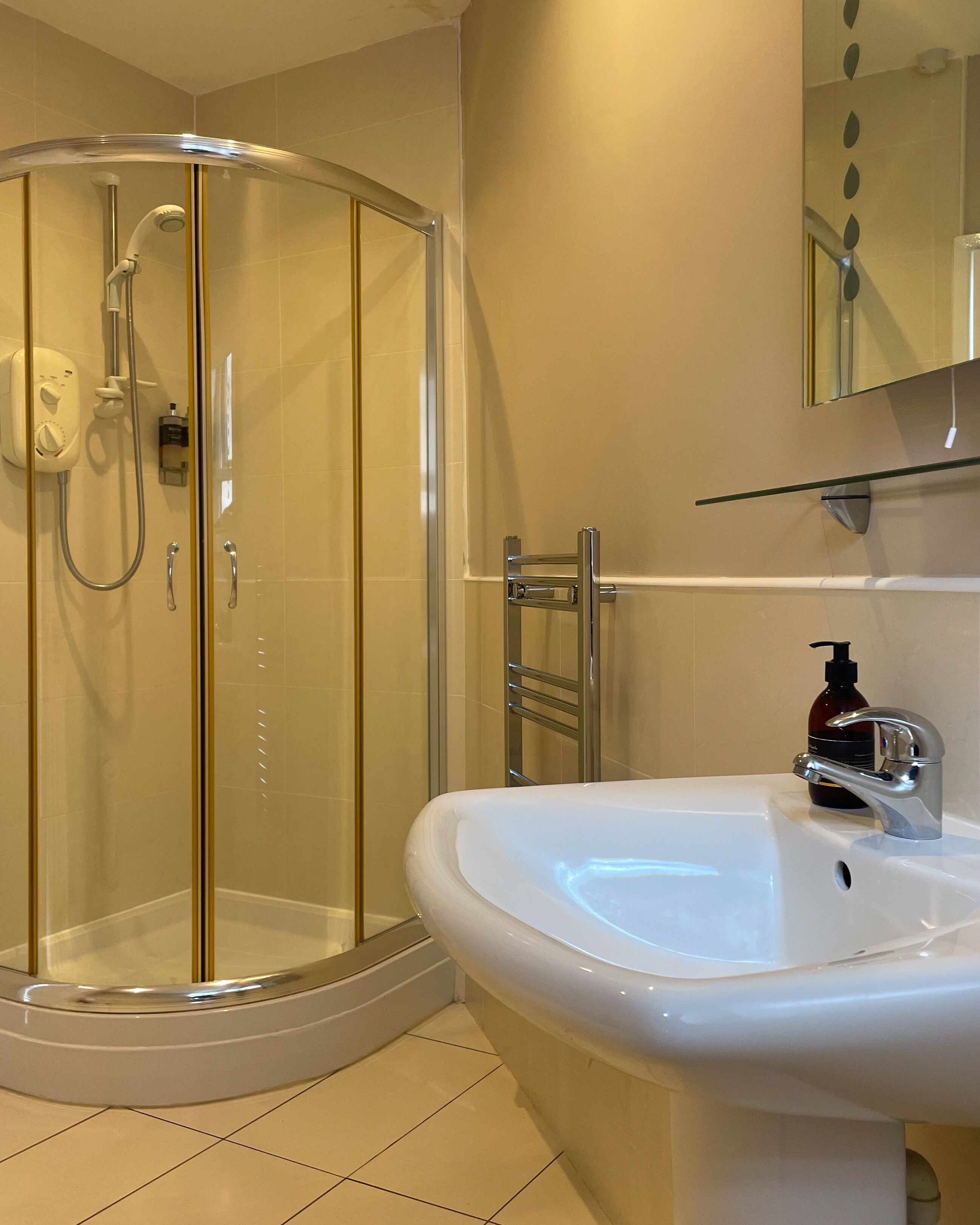 Une salle de bain moderne avec une douche à parois de verre, un lavabo blanc doté d’un robinet chromé et un miroir au-dessus du lavabo.