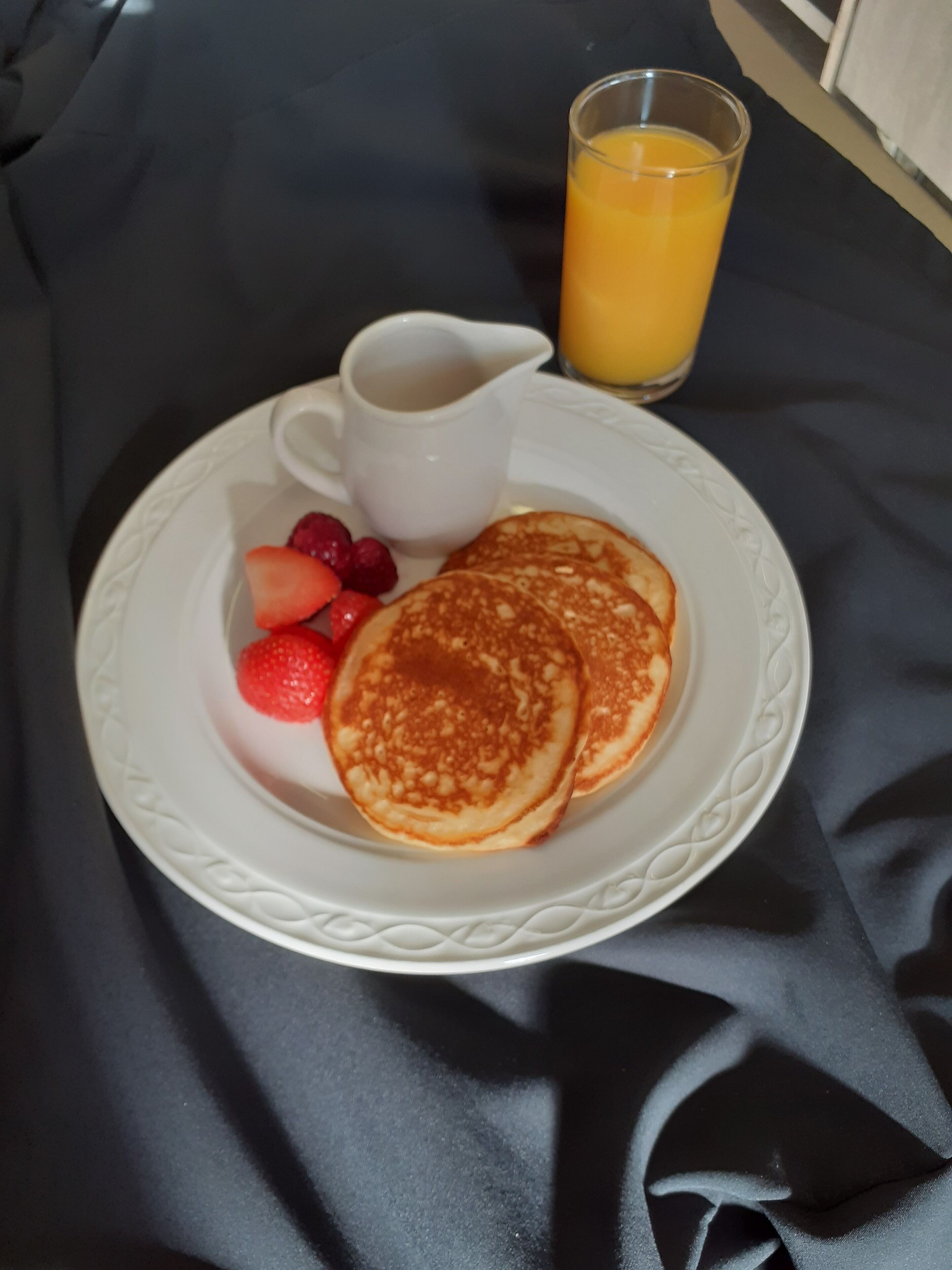 A plate with pancakes, strawberries, and a glass of orange juice on a dark tablecloth.