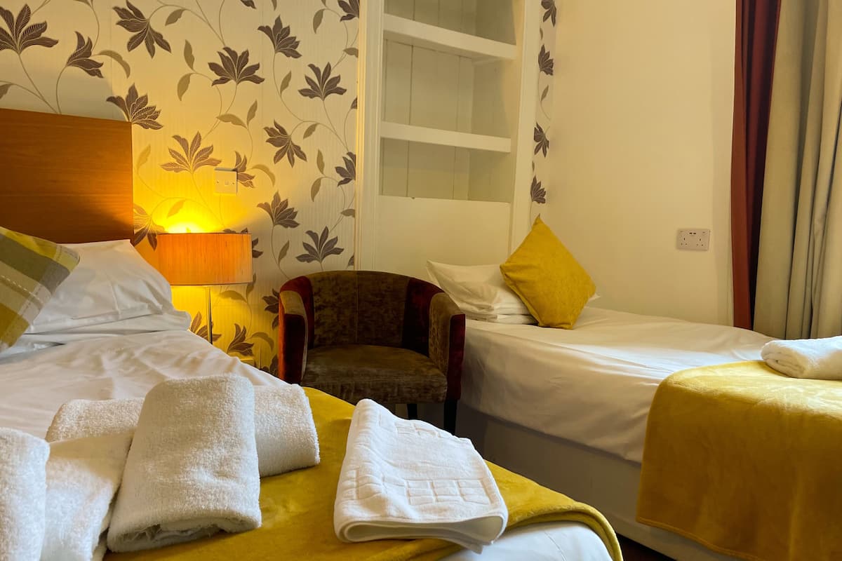 A hotel room with two beds, a chair, and a lamp.