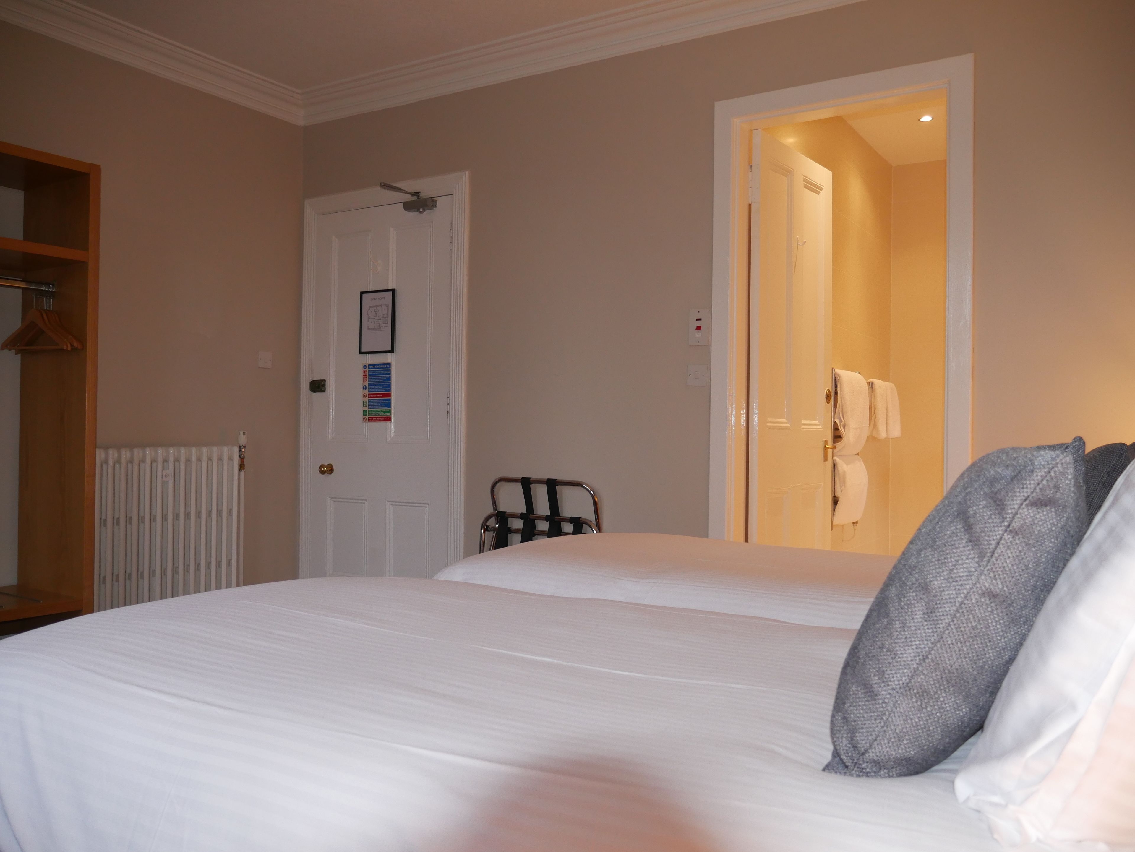 A hotel room with a bed, a radiator, a door with a sign, and a towel rack.