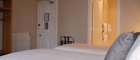A hotel room with a bed, a radiator, a door with a sign, and a towel rack.