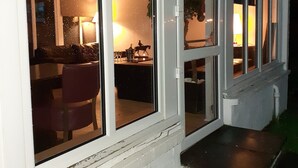 A house with large windows, a visible kitchen area, and a small outdoor seating area.