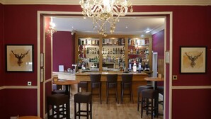 A bar area with wooden flooring, bar stools, a chandelier, and a well-stocked liquor shelf.
