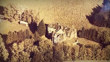 An aerial view of a large, historic building with multiple wings, surrounded by dense forest.