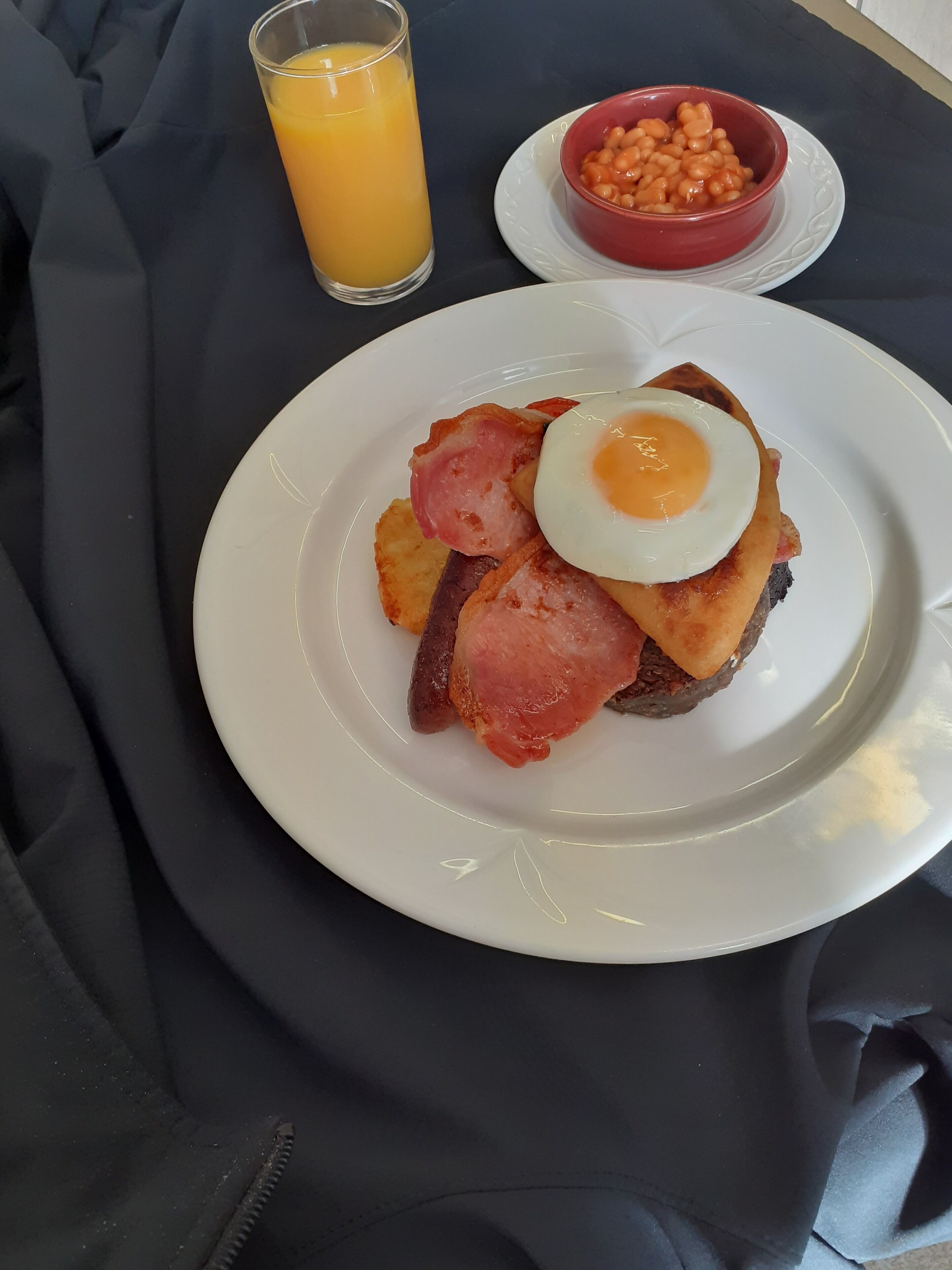 Un plato de desayuno con huevos, tocino, tostadas, un vaso de jugo de naranja y un tazón de frijoles horneados sobre una mesa.