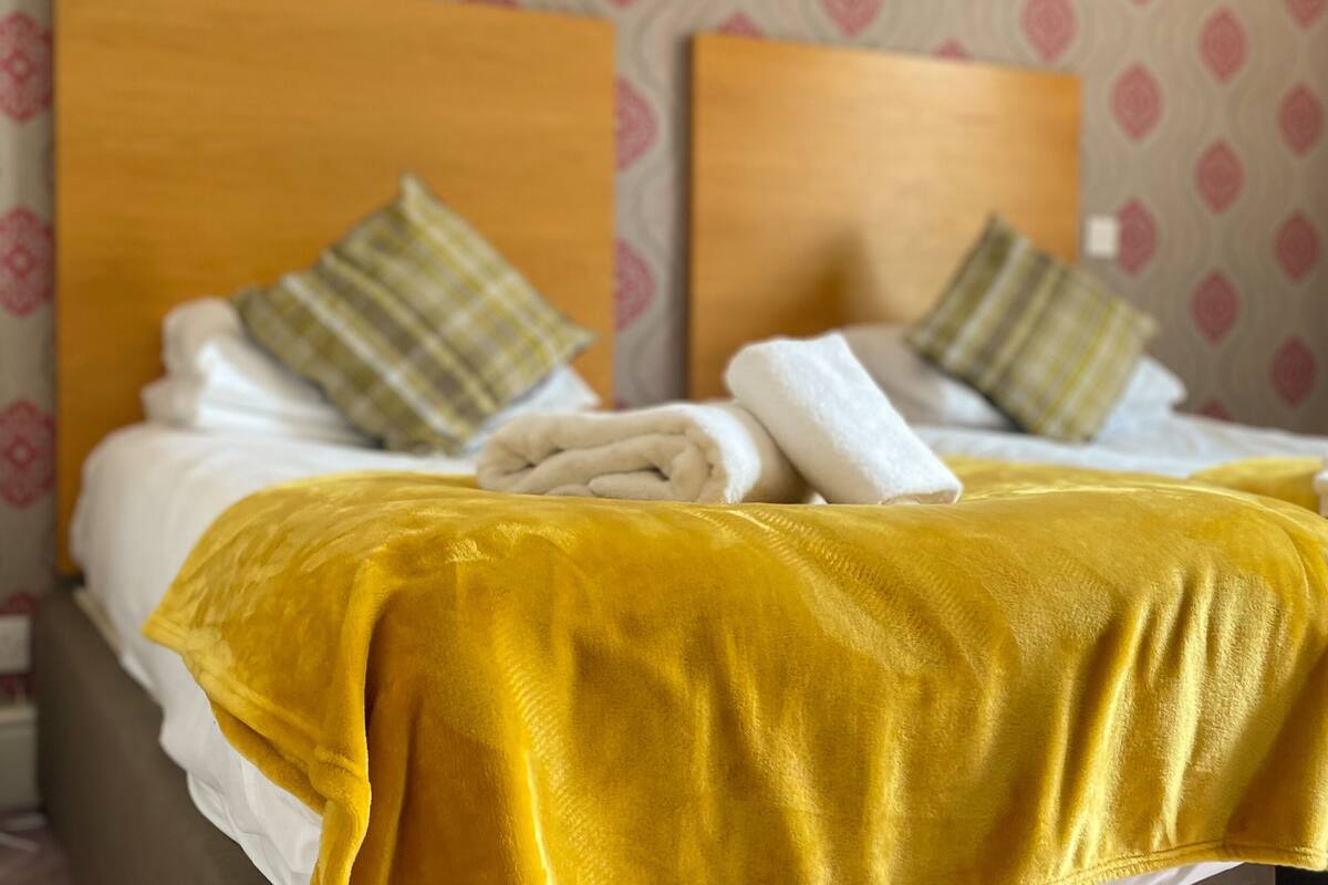 A hotel room with two beds, each with a wooden headboard, white linens, and a yellow throw blanket.