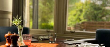 A dining table with a vase of flowers, salt and pepper shakers, a glass of water, and a plate with cutlery.