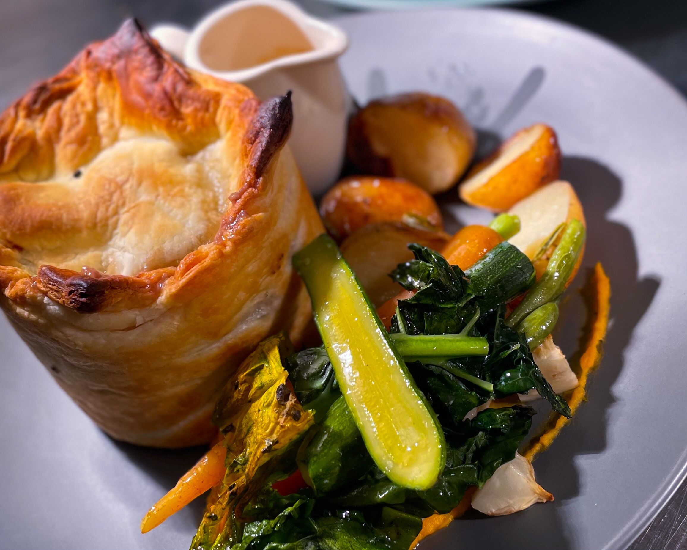 A meal consisting of a pie, roasted vegetables, and a side of greens.