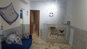 A small, cozy room with a blue sofa, a small table with a sign reading "B&J Jetsons", a welcome sign, and a netted decoration on the wall. - Nettuno (Messina)