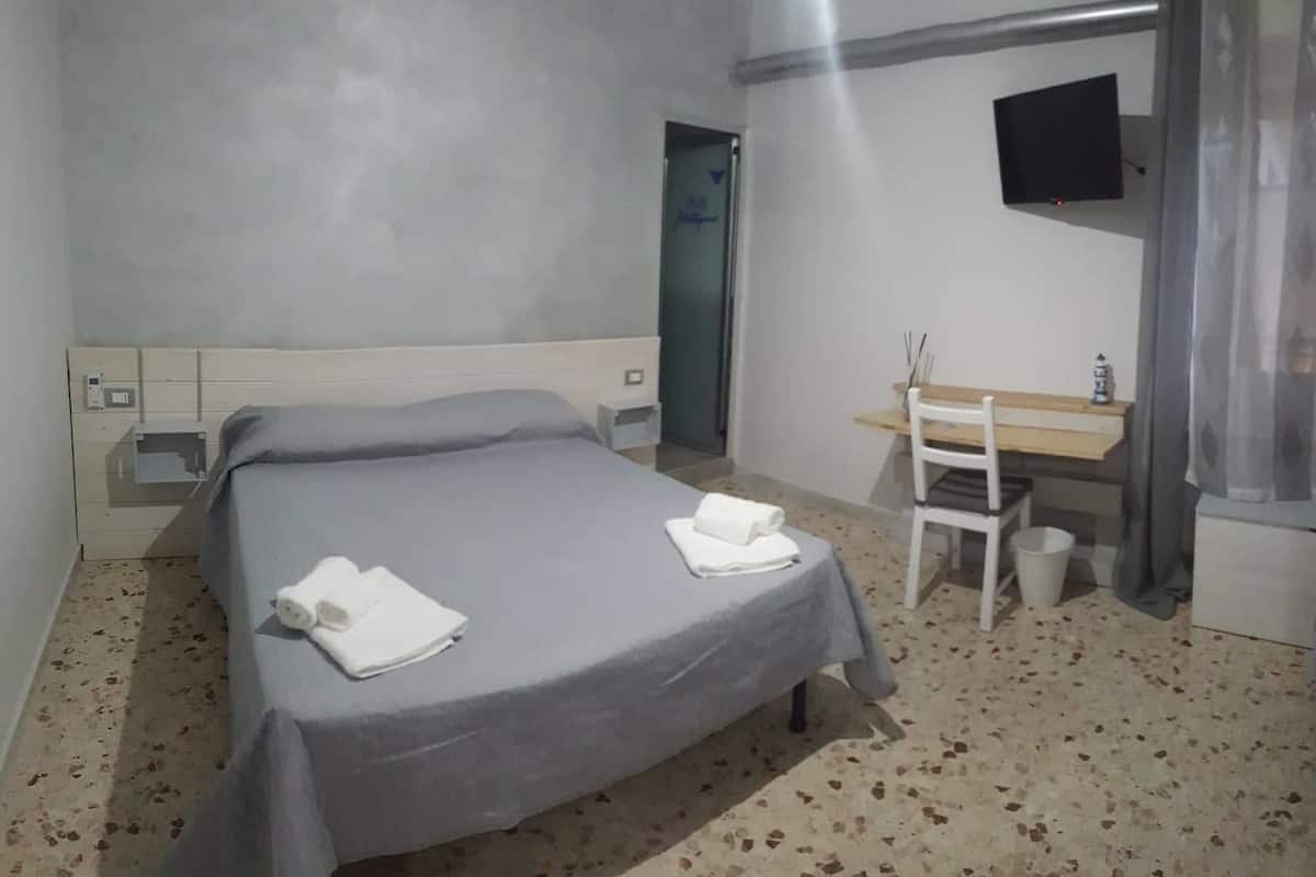A bedroom with a bed, a desk, a chair, and a TV.