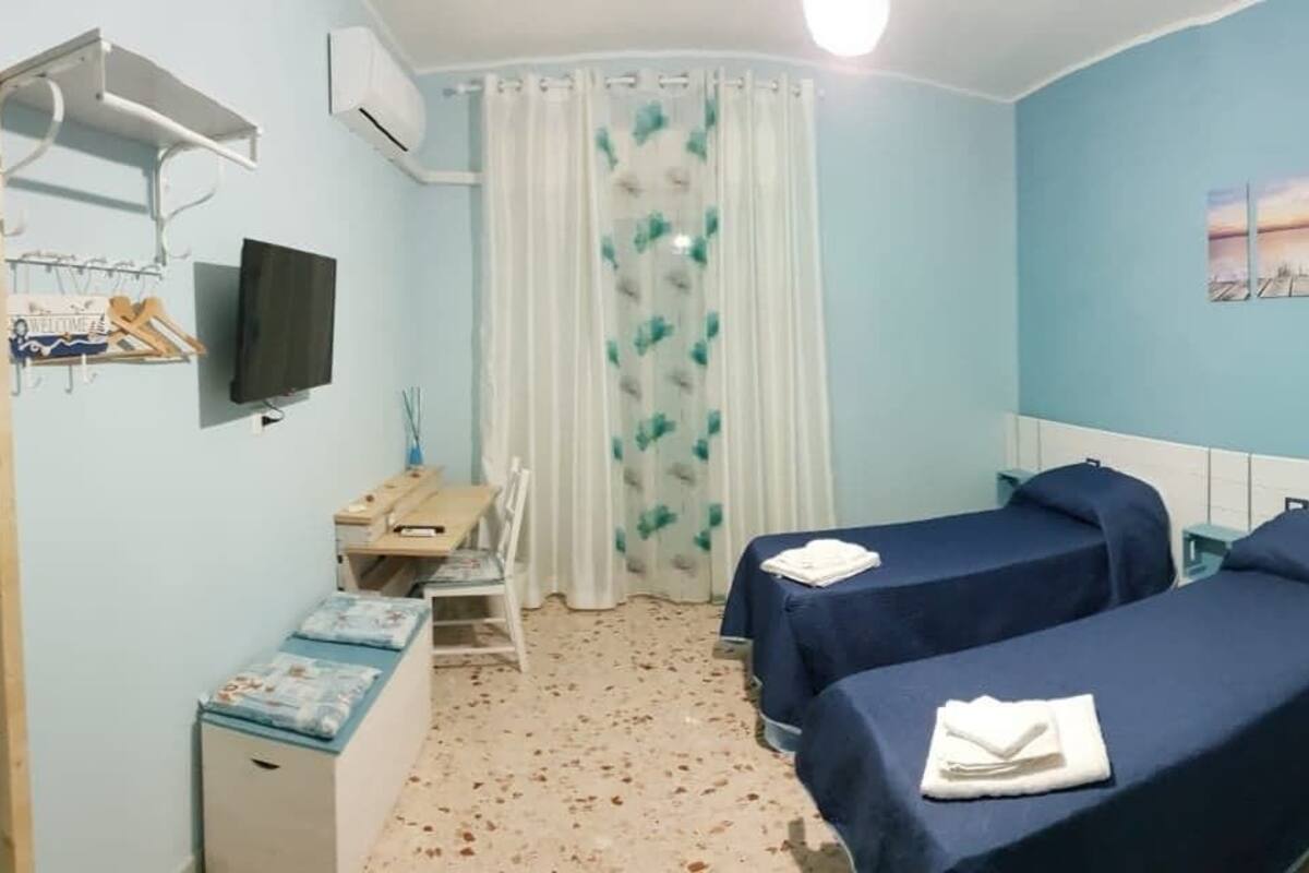 A hotel room with two beds, a desk with a chair, a TV, and a window with curtains.