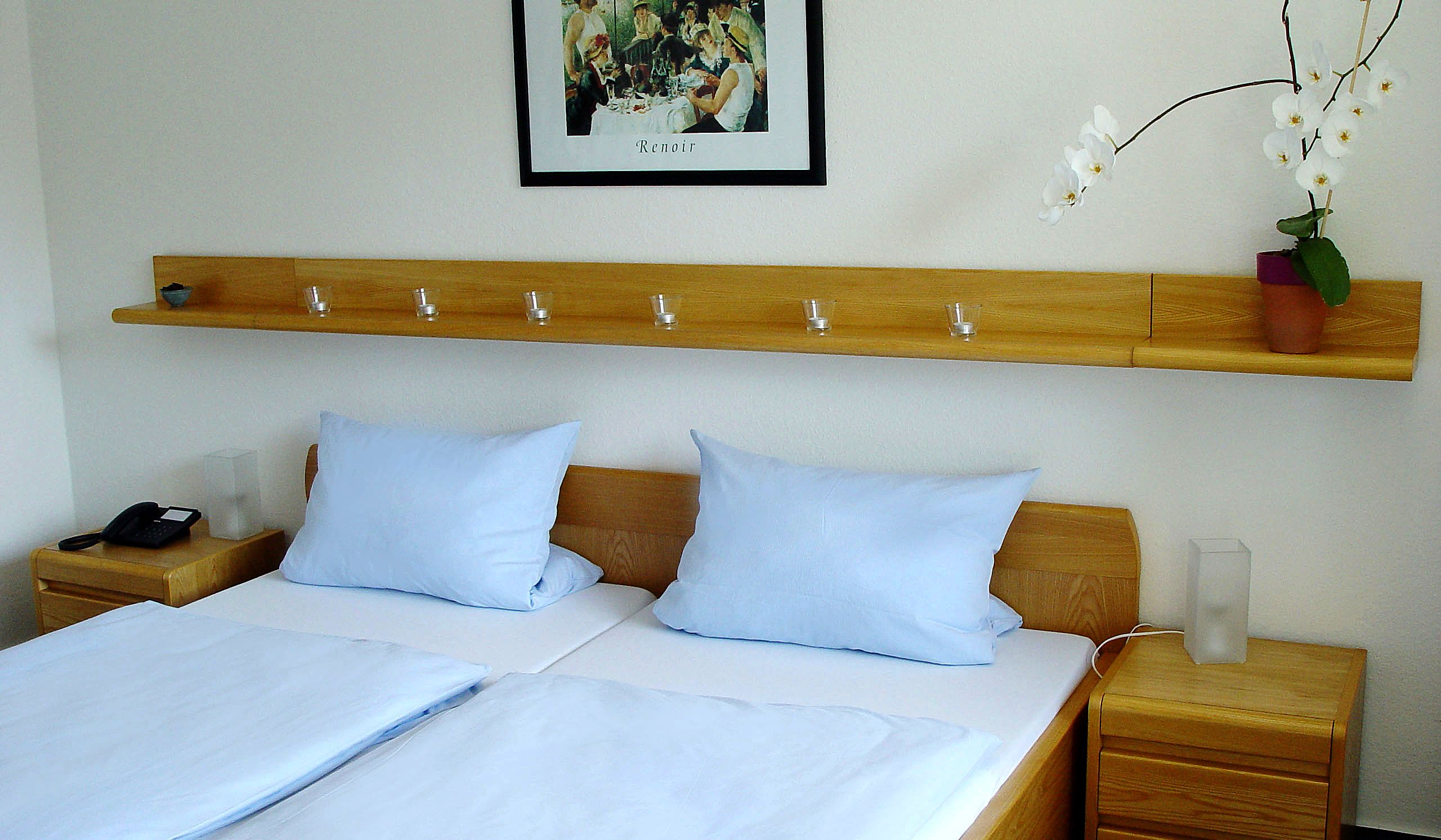 A double bed with two pillows, a bedside table with a phone and a glass, and a nightstand with a lamp.