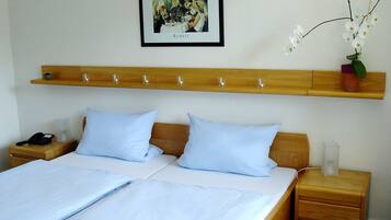 A double bed with two pillows, a bedside table with a phone and a glass, and a nightstand with a lamp.
