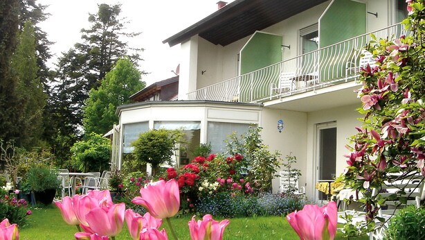 A two-story building with a balcony, surrounded by a garden with pink tulips and various other plants. - Hotel Ebnet Garni (Lindau)
