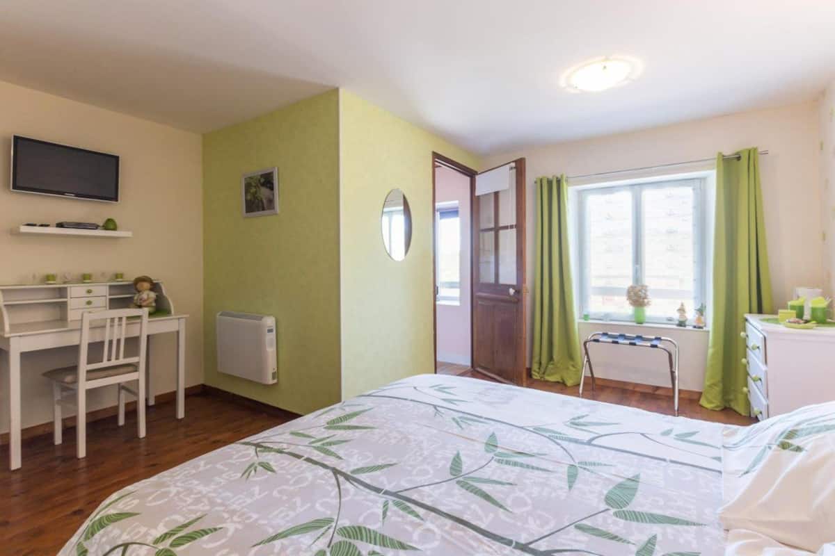 Une chambre à coucher comprenant un lit, un bureau, une chaise, un téléviseur et une fenêtre avec des rideaux.